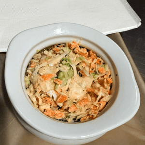 Creamy shredded coleslaw (cabbage and carrot) in a light blue bowl on a metal tray with a napkin nearby.