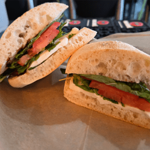 Two halves of a crusty baguette sandwich filled with mozzarella, tomato, and fresh greens on a wooden board