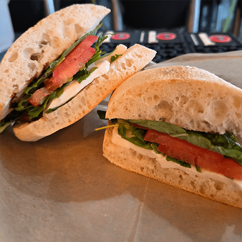 Two halves of a crusty baguette sandwich filled with mozzarella, tomato, and fresh greens on a wooden board